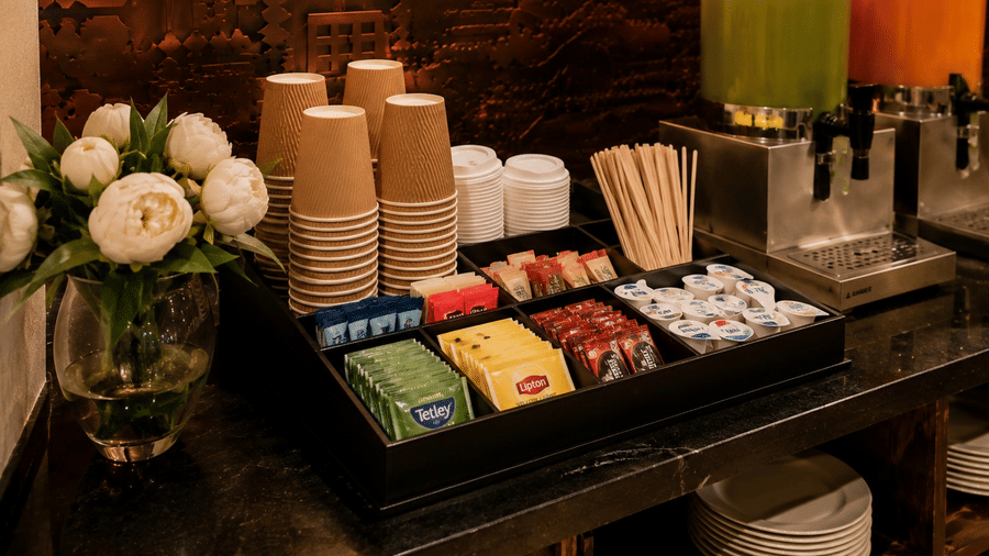 Tea and coffee station at Lime Tree Hotel & Banquet, Jaipur, showing paper cups, assorted tea bags, condiments, and juice dispensers.