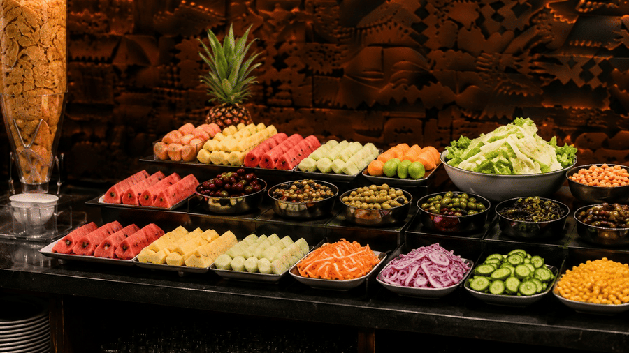 A buffet counter at Lime Tree Hotel & Banquet, Jaipur, displaying platters of sliced fresh fruits, chopped vegetables, and a whole pineapple.