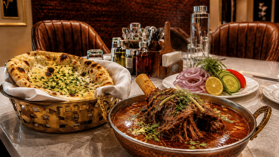 A dining table set at Lime Tree Hotel & Banquet, Jaipur, featuring a large bowl of meat curry, a basket of naan bread, and a side salad.