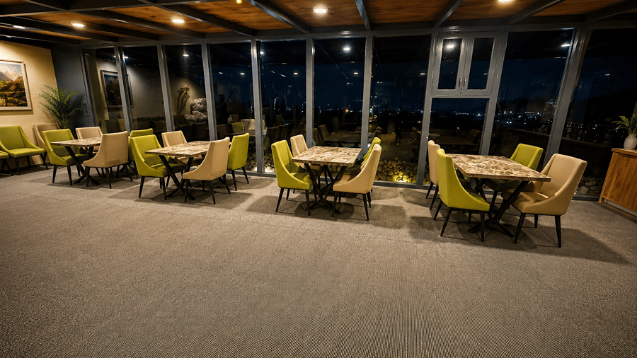 Indoor seating area with multiple tables and chairs, warm ceiling lighting and large windows overlooking the night-time surroundings.