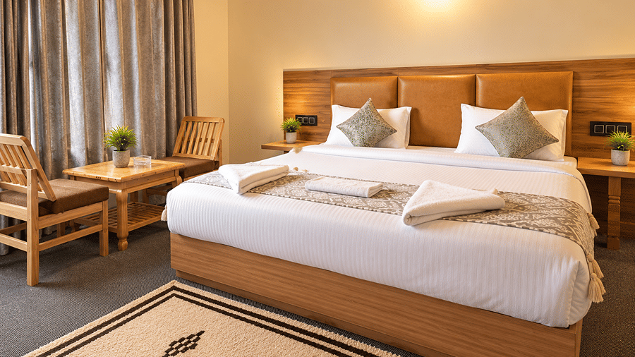 Bedroom with a queen-size bed, patterned floor rug, wooden seating area and large window overlooking the mountain landscape.