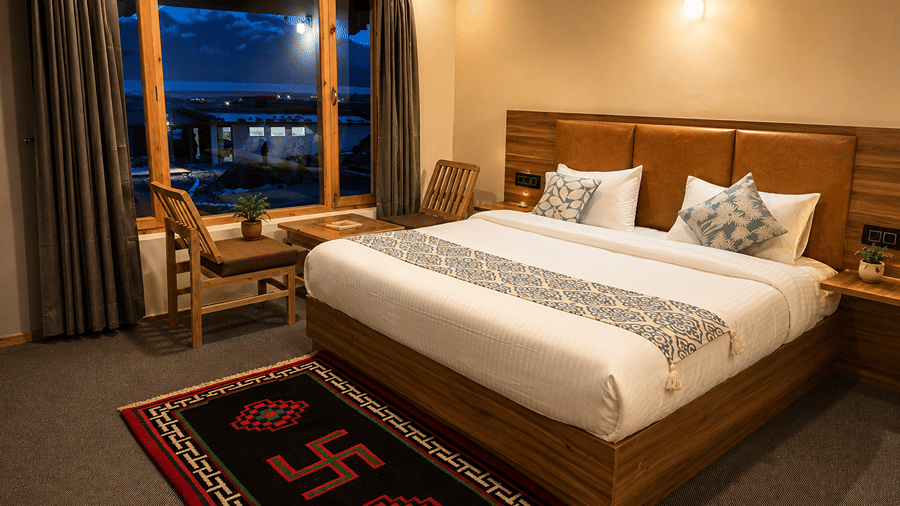 Bedroom with a queen-size bed, wooden headboard, bedside tables and a large window overlooking the illuminated night-time landscape.