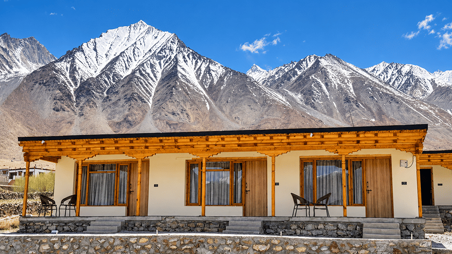 Facade of Royal Rebo Pangong with wooden balconies and large windows, set against snow-covered mountains and a blue sky.