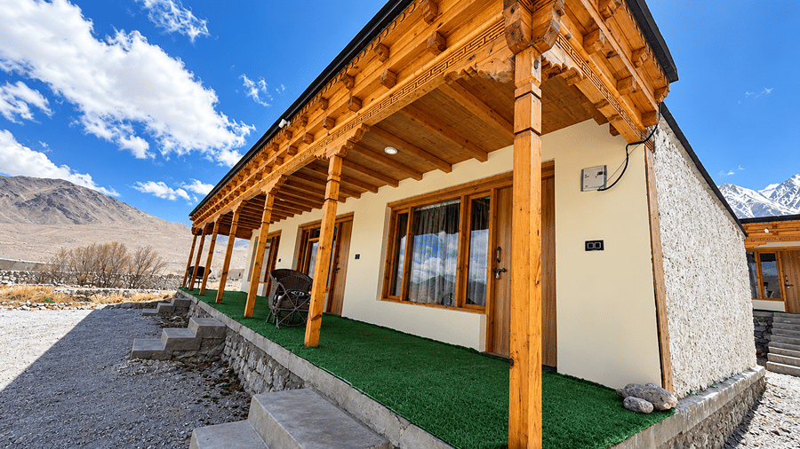 Exterior of the property with wooden balconies, large windows, stone pathway and snow-covered mountains in the background.