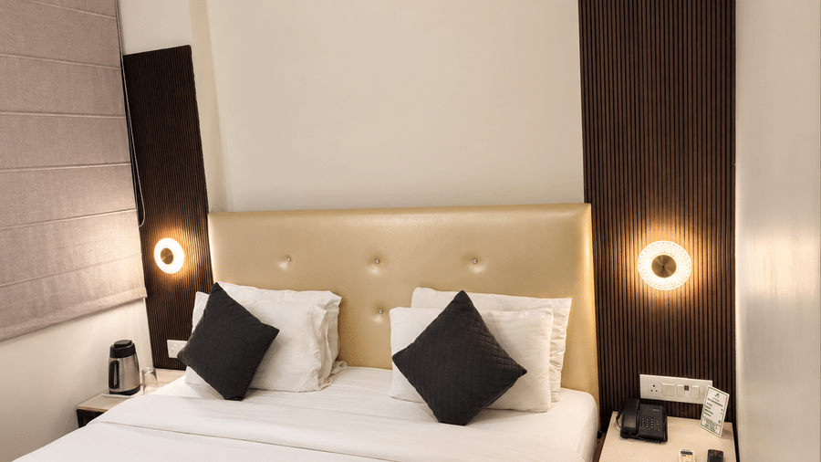 Studio Room at TGI Apple Inn, Ajmer Road, Jaipur featuring a bed with pillows, lamps on the wall, and a bedside table.