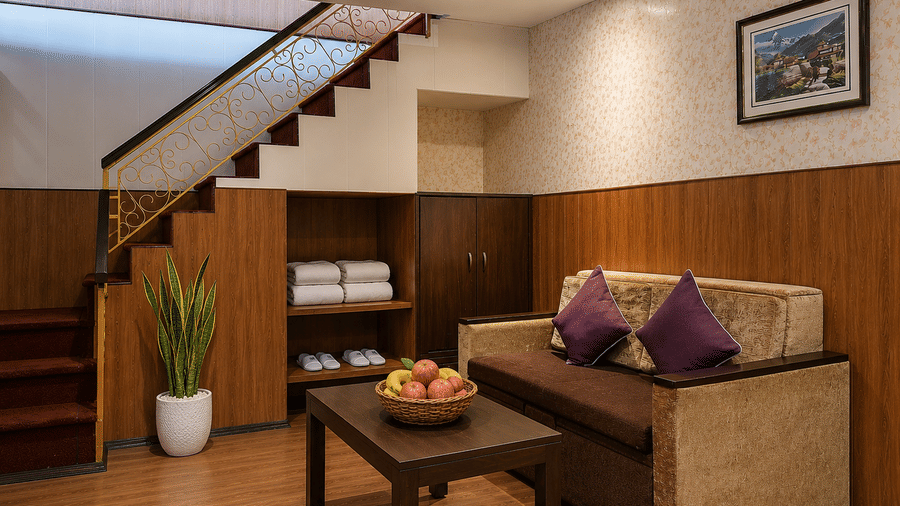 Living room at Valmere Thistle Boutique Hotel, Darjeeling with a wooden staircase, a sofa with purple cushions, and built-in shelves with towels.Valmere Thistle Living room