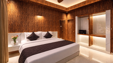 Front view of the Superior Room at Shakuntalam Hotels featuring a king bed with dark and white bedding wooden wall panels ceiling fan warm floor lighting and a marble accent wall.
