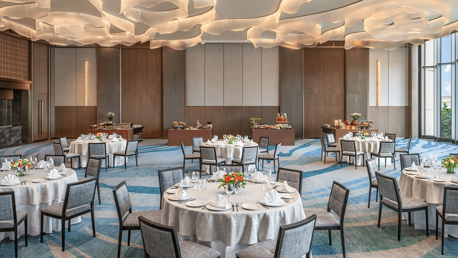 The well-lit Ballroom 2 with round dining tables, wave-patterned blue carpet, and unique cloud-like ceiling fixtures at The Residency Towers Chennai.