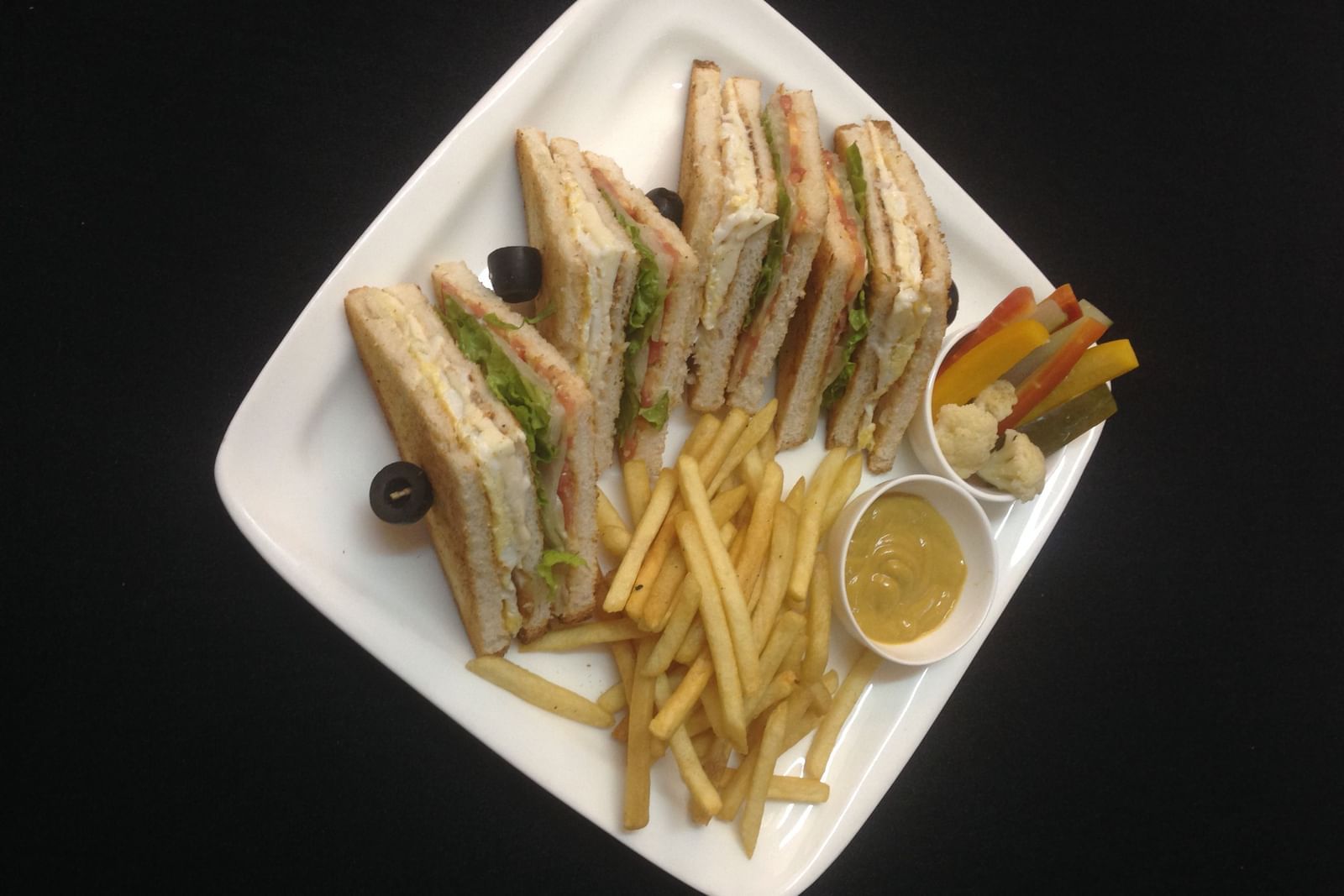 Club sandwiches served with golden french fries and black olives on a white plate | Daksh The Madhuvan Suites