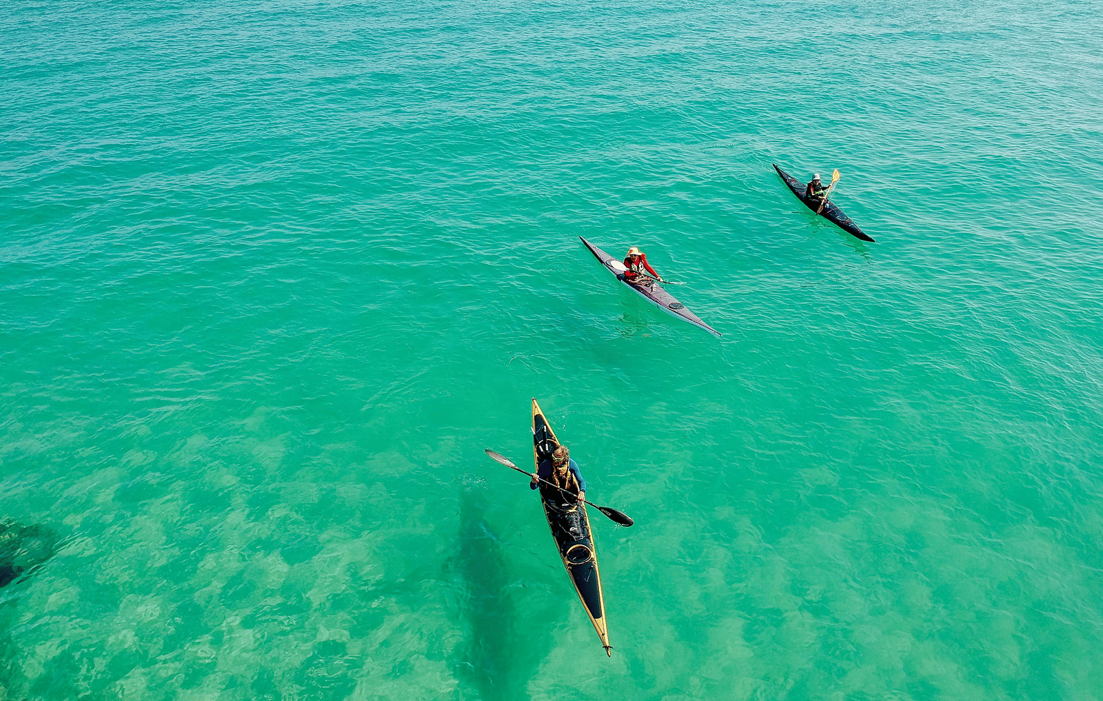 Kayakers paddling over clear turquoise water, with the sea floor faintly visible below.