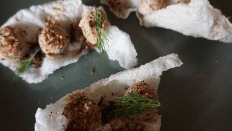 Fine dining Newari fusion appetizer served on crisp rice crackers at a boutique restaurant in Kathmandu, Nepal.