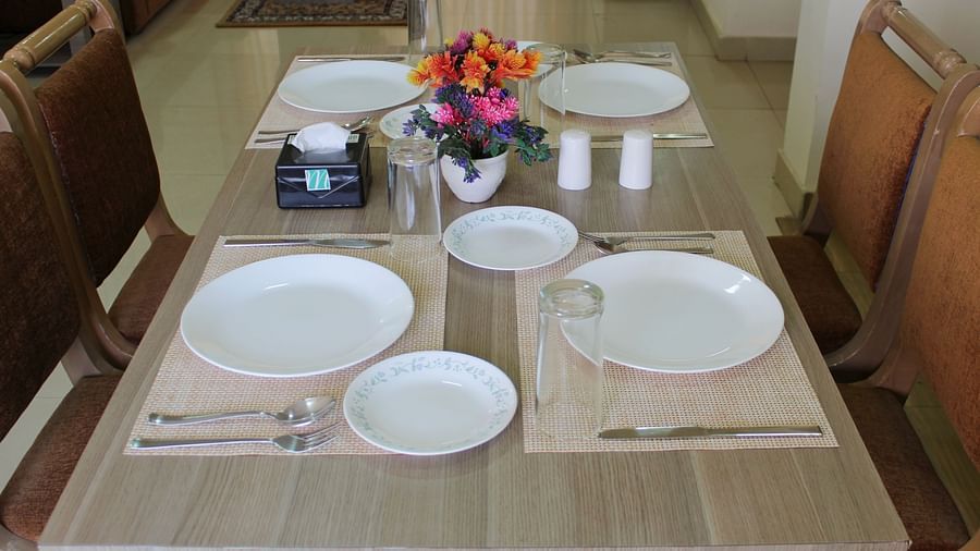 A close shot of the rectangular dining table with cutlery on it and four brown chairs around it