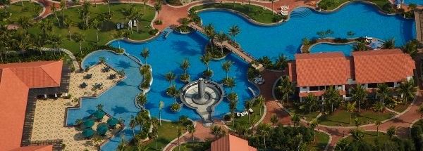 An aerial view of Hotel Mamallaa Heritage, Mahabalipuram, showing multiple red-roofed buildings, greenery, winding paths and pools.