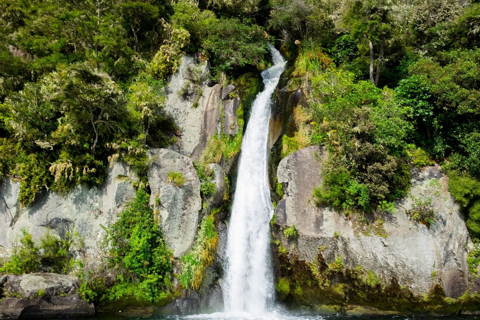 an overview of a waterfall getting collected into a waterbody with blue sky in the background.