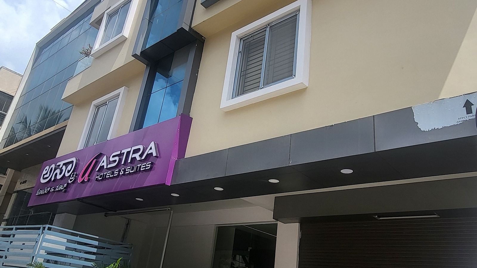 The exterior of a modern hotel building with multiple floors, large windows, and a bright blue sky in the background - Astra Hotels and Suites, HSR Sector 7