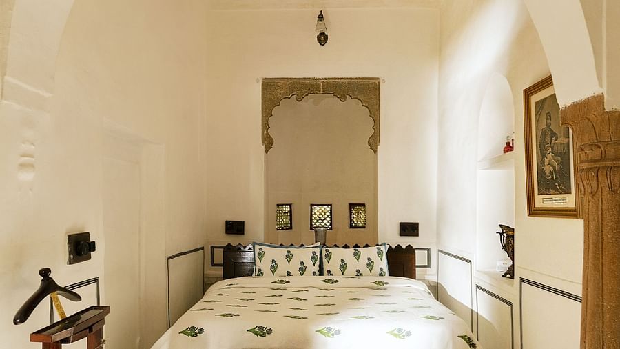 A bright bedroom at Fort Barli, featuring a white arched doorway and a patterned bed, offers a minimalist yet elegant sleeping space.