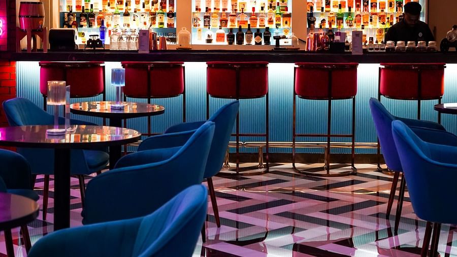 Modern bar interior with vibrant lighting highlighting a full array of spirits on shelves, sleek bar stools, and a reflective tile floor.