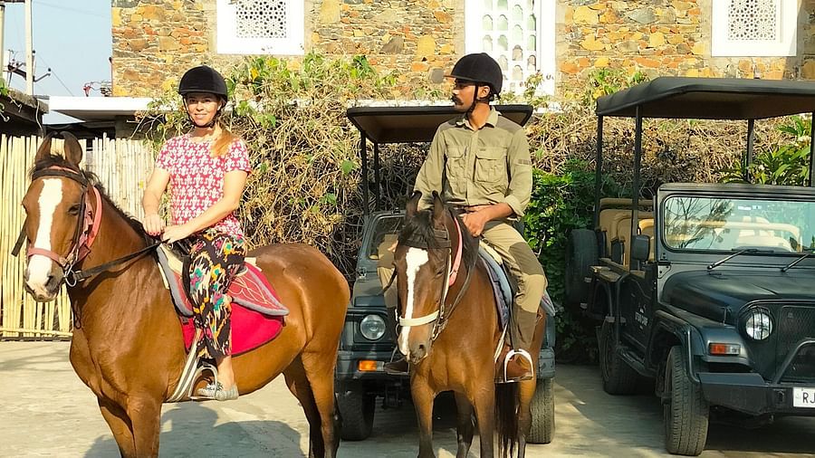 An image of a man and woman riding two horses with the backdrop of the hotel - Utsav Camp Sariska
