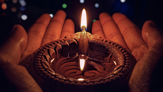 Hand holding a traditional clay lamp with colourful lights glowing softly in the background during Diwali in Chennai