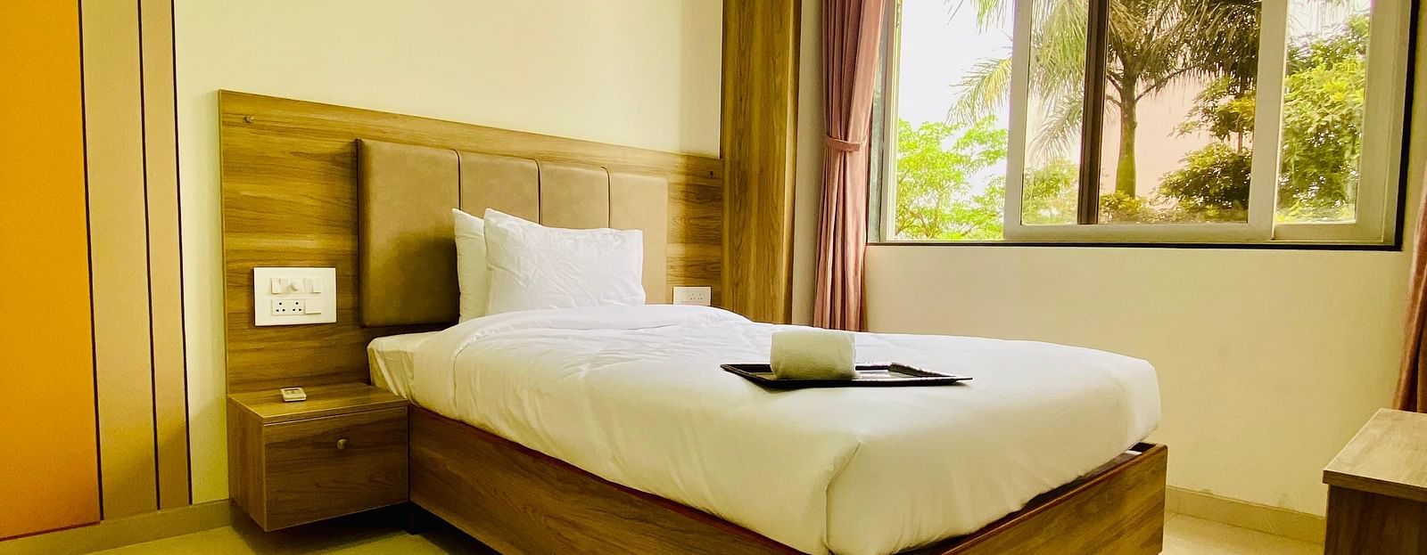 A bright hotel room featuring a neatly made bed, large windows, and a peaceful view of the outdoors.