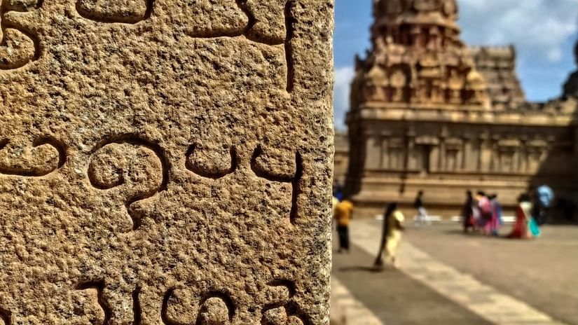 A close up of the scriptures on a wall in Thanjavur with a temple in the background.