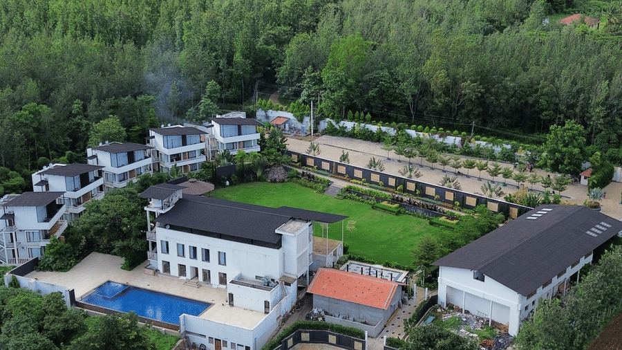 Resort buildings, swimming pool, and an open courtyard surrounded by dense green forest and mountains under a cloudy sky at Bindiga Peak Resort.