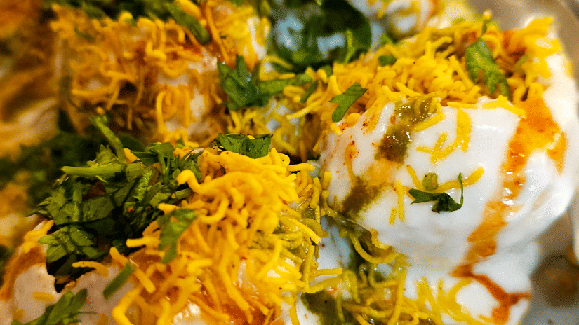 Plate of dahi puri topped with yoghurt, sev, chutneys, and fresh coriander served at a casual dining venue