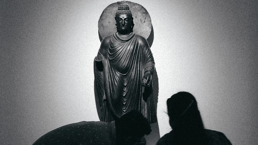 A sculpture of Buddha displayed at a museum and people standing in front of it