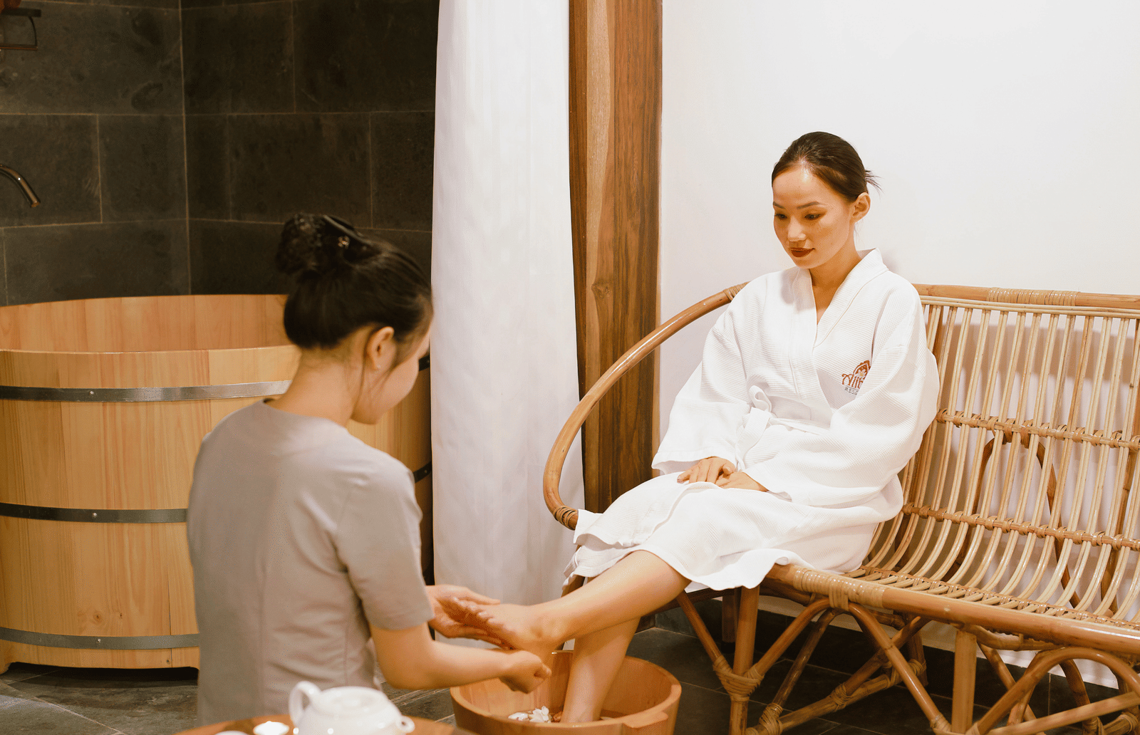 A woman receiving pedicure by another woman in a wooden furnished room in at Alibu Resort - Vietnam seaside resorts