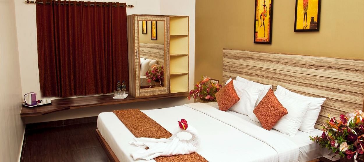 Flora Suite at TGI Star Holiday Resort, Salem Main Road, Yercaud featuring a plush bed with a towel art on it under warm lighting and bouquet on the nightstands on both sides 