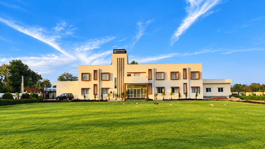Cream-coloured hotel building surrounded by a spacious green lawn under a blue sky.