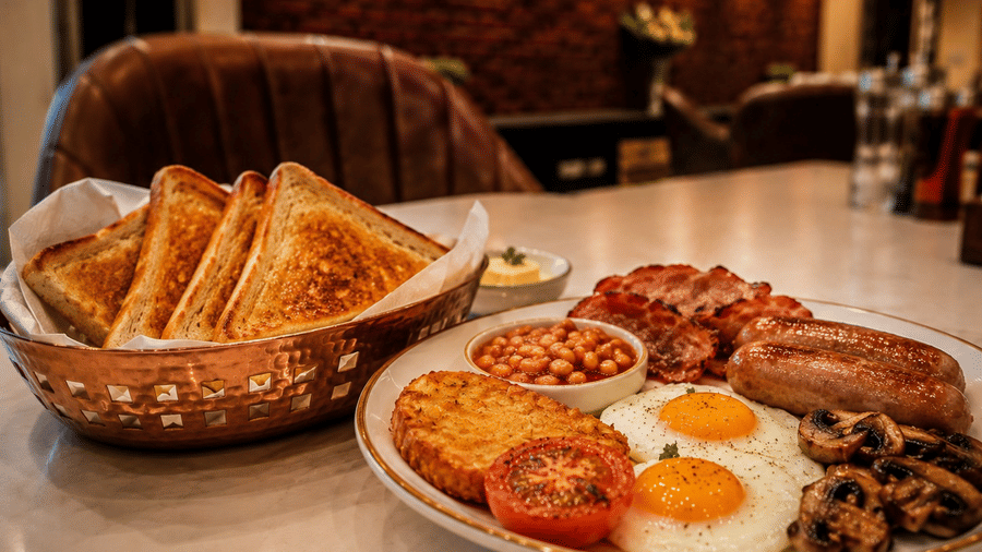 Breakfast served at Lime Tree Hotel & Banquet, Jaipur, featuring fried eggs, sausages, baked beans, a hash brown, tomatoes, and toasted bread.