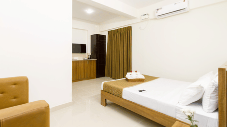 Hotel room with a single bed, a sofa, an air conditioner, and floor-length wooden curtains at Sanctum Suites Whitefield, Bangalore.
