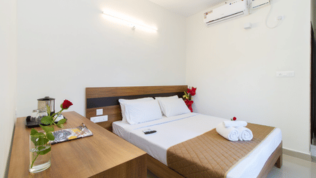 Hotel room with twin beds, white linen, wooden headboards, and an air conditioner at Sanctum Suites Whitefield, Bangalore.