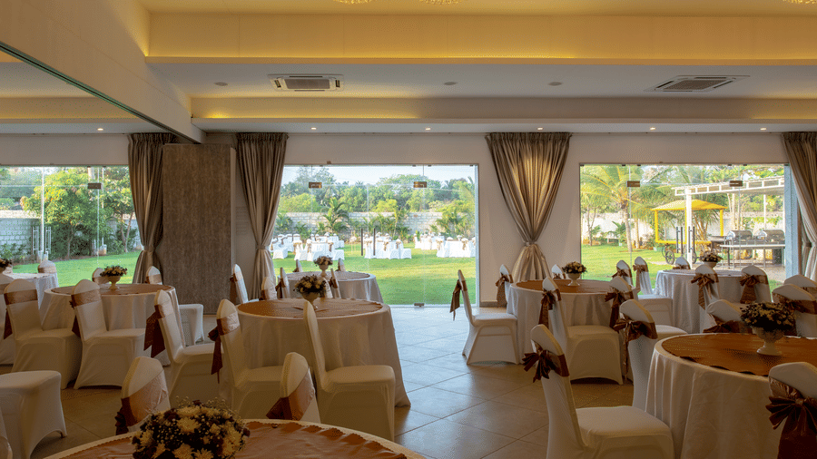 An indoor banquet hall with round tables and chairs draped in white with brown sashes, set for an event - Grande Bay Resort & Spa, Mamallapuram