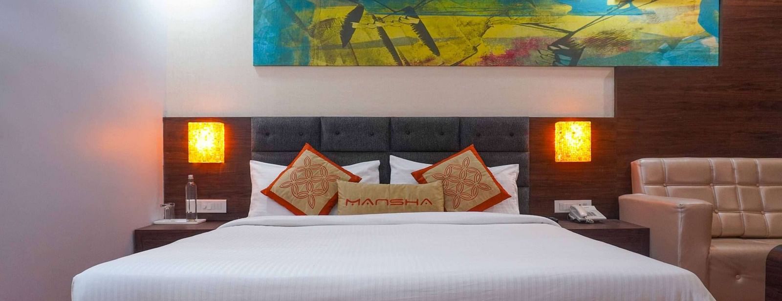 A room with a king size bed, bed side tables, lamps, and a sofa at Mansha Hotel Regency.