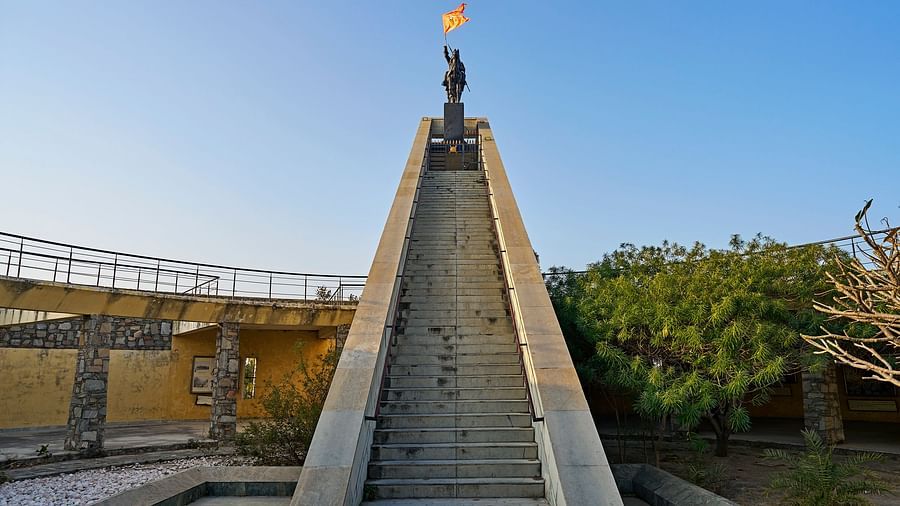 image featuring a statue holding an orange flag towards which the steps are leading to at the top at dev shree, deogarh