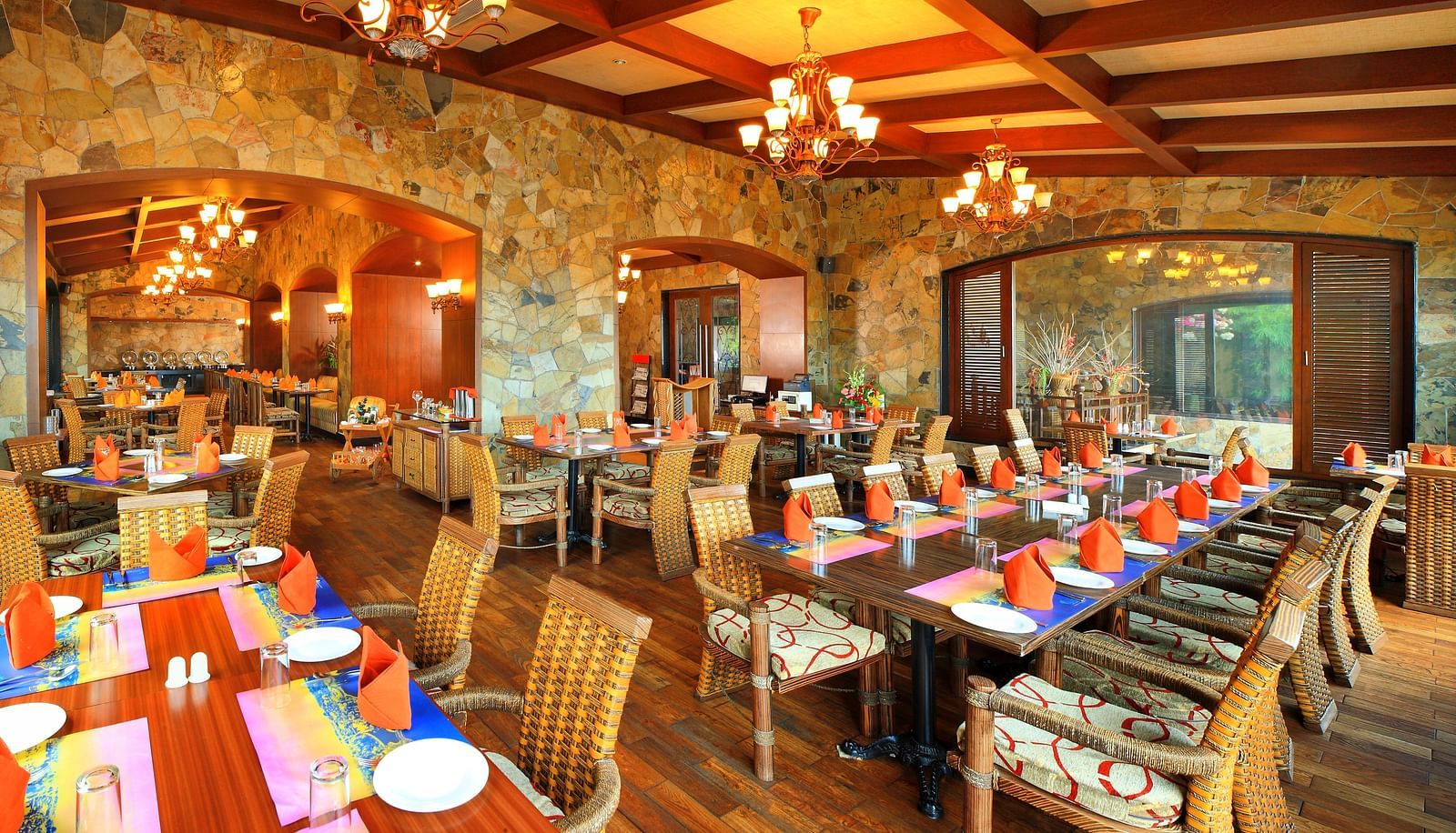 Amber restaurant at Ocean Spray Puducherry featuring wooden tables and chairs set, plates, cutlery, mat, and hand towels are placed on the table