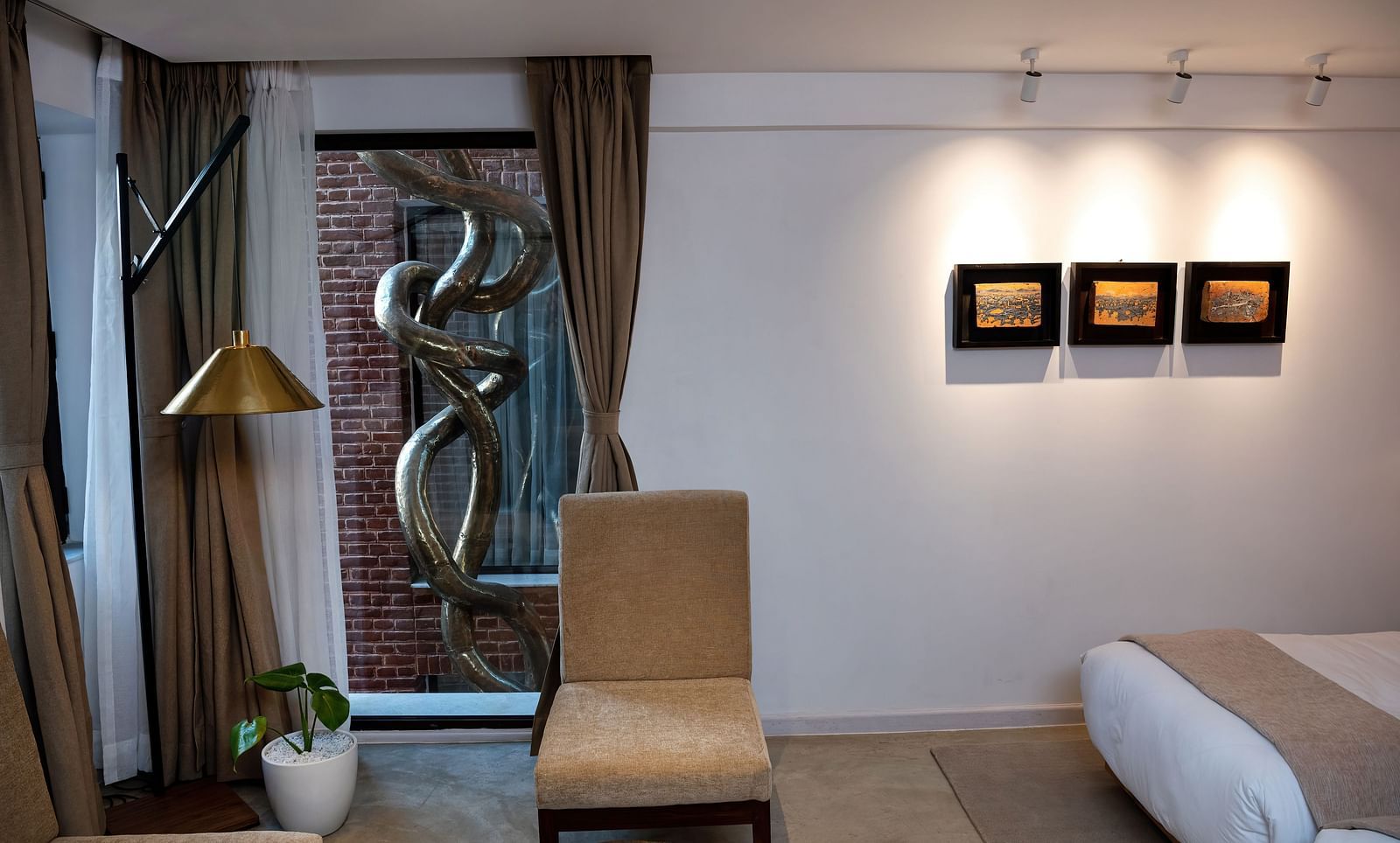 A room with a bed, chair, lamp, three pieces of art work hung on the wall, and a window overlooking the infinity loop - The Nanee