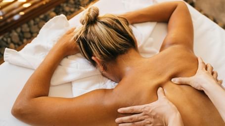 A top-down shot of a person receiving a back massage on a massage table, with the masseuse's hands applying pressure to their back.