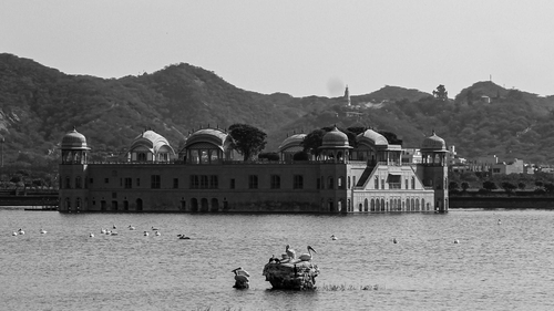 View of a Palace in the middle of a lake with mountains and clear blue sky in the background.