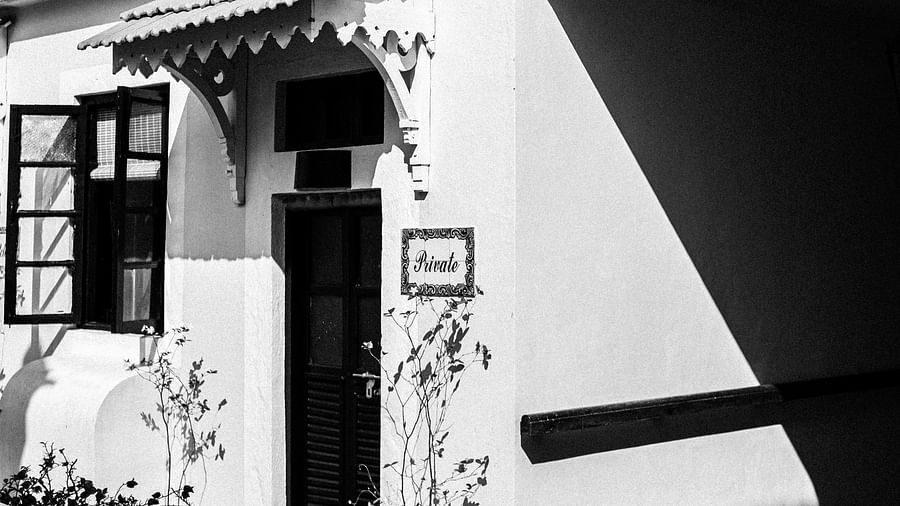 A black and white image of a white building with dark windows and a balcony, showcasing intricate architectural details and strong shadows at Fort Tiracol, Goa.