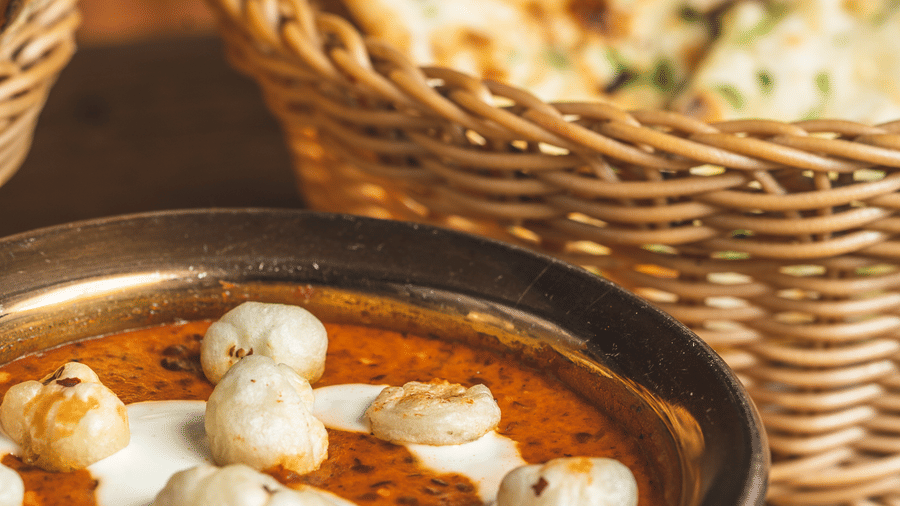 Close-up of Indian curry in a copper bowl, topped with cream, next to a basket of Naan at Hotel Hukam's Lalit Mahal.