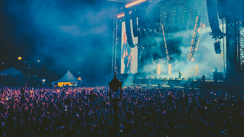 Open-air concert stage lit up at night with a cheering crowd in front