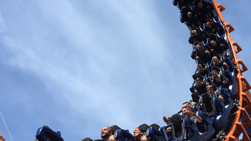 people sitting in a roller coaster while its travelling with blue sky in the background