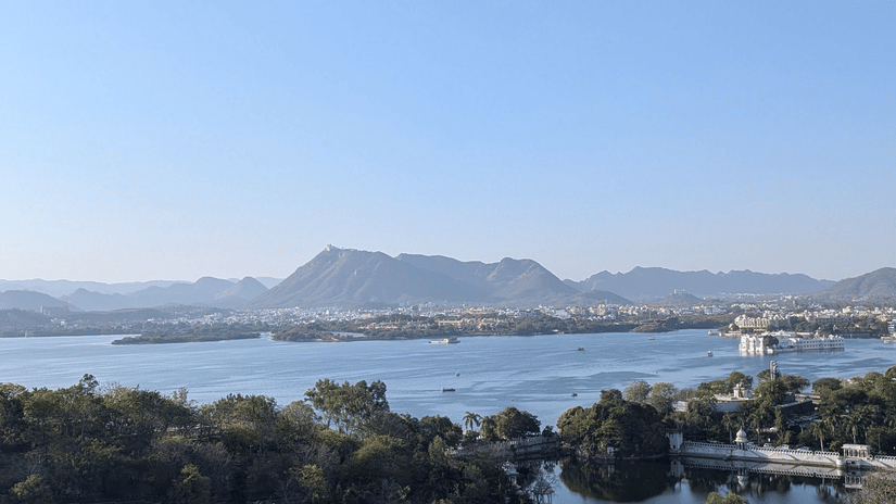 Captivating aerial view of Udaipur's serene lake and lush greenery under clear skies.