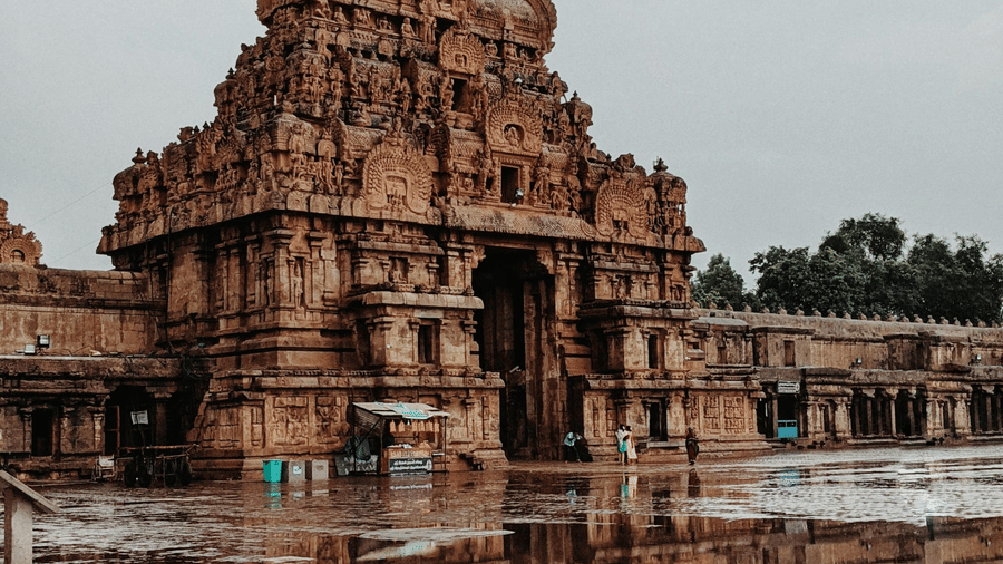 An ornate stone temple gateway reflected beautifully in a large puddle on the wet ground after rainfall