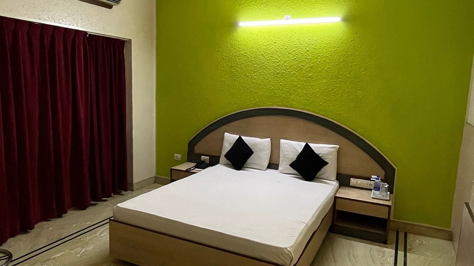 a corner view image of the standard room featuring a double bed against a green coloured wall at The Grand Krishna Rooms, Bengaluru
