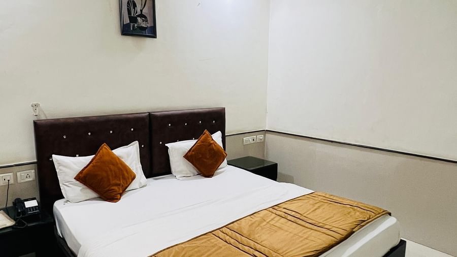 A cozy hotel bedroom with a neatly made bed and dark wooden furniture | Deluxe Room | Hotel Aadhar