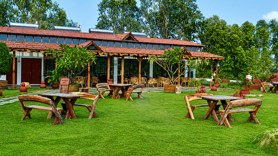 Paanam - The Bar outdoor lawn seating with wooden picnic tables and lush greenery, offering a relaxing open-air spot to unwind
